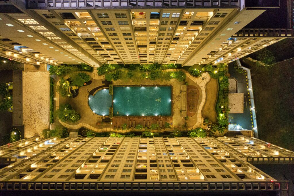 Captivating aerial view of illuminated modern urban buildings surrounding a swimming pool at night.